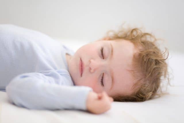 Red haired baby in light blue long sleeved onesie sleeps during the day.