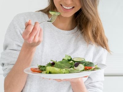Healthy mom holding plate of green salad ready to take a bite.